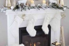 a snowy Christmas mantel with deer, candles, shiny Christmas trees, a snowy evergreen garland with pinecones