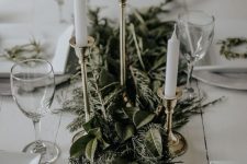 a sophisticated Christmas table with a lush greenery table runner, tall and thin candles and neutral porcelain is a chic idea