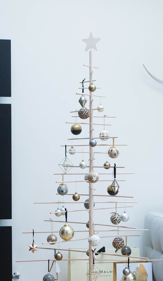 a stick Christmas tree with various metallic and color block and shiny ornaments is a creative modern alternative to a usual Christmas tree