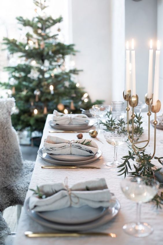 a stylish Christmas tablescape with grey plates, neutral linens, greenery, a tall brass candelabra with tall and thin candles