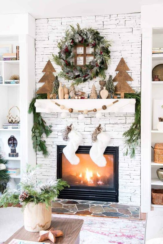 a stylish Scandi Christmas mantel with wooden trees, vases, a wooden bead garland, an evergreen and pinecone wreath plus stockings