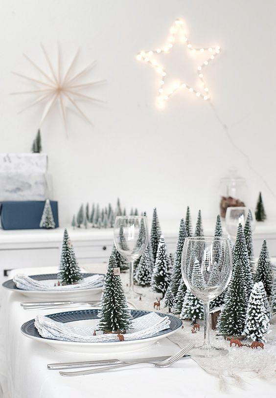a stylish neutral Christmas table setting with flocked Christmas trees as a centerpiece and on each place setting, blue plates