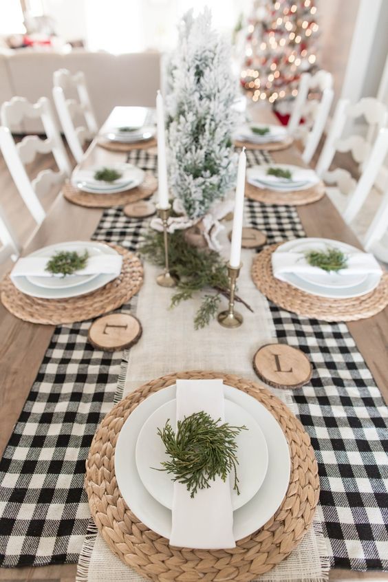 a stylish neutral Christmas tablescape with a buffalo check runner, woven placemats, tan and tall candles, greenery and flocked mini trees