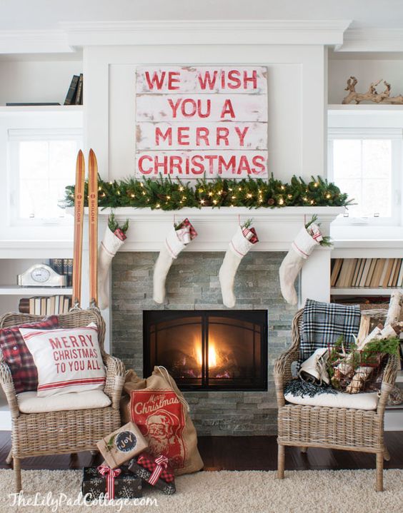 a traditional Christmas mantel with a light evergreen garland, white stockings, a sign, skis and some plaid touches here and there