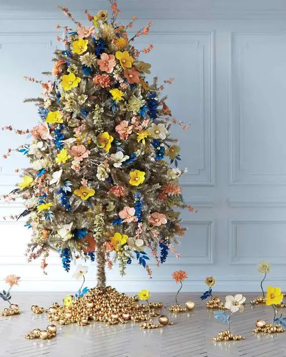a unique gold Christmas tree decorated with yellow, blush, electric blue faux flowers and blooming branches and with bells on the base