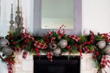 a vintage farmhouse Christmas mantel with an evergreen, oversized bell and red plaid ribbon garland, metal candleholders and gift boxes