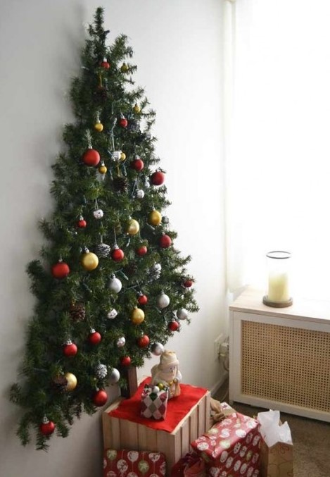 a wall mounted Christmas tree with pine garlands and Christmas ornaments plus pinecones looks natural and cool