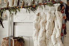 a whimsy Christmas mantel with an evergreen and dried fruit slice garland, mini Christmas trees and oversized white stockings