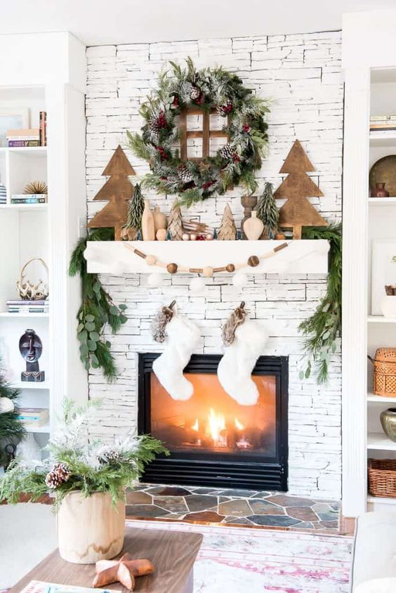 a woodland Christmas mantel with wooden Christmas trees, vases, wooden beads, an evergreen wreath and a garland plus white stockings