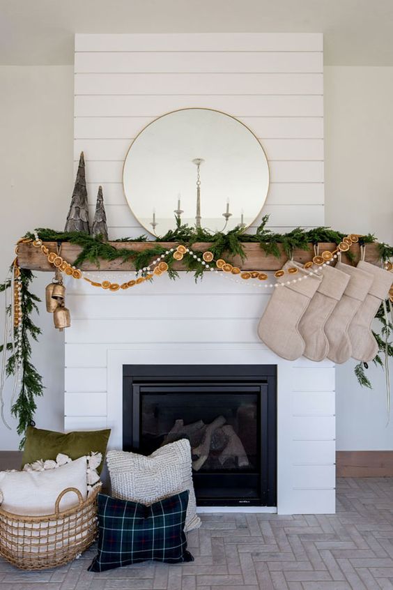 an all natural Christmas mantel with an evergreen garland, a dried citrus garland and pompoms, burlap stockings and oversized bells