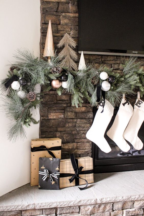 an elegant modern Christmas mantel with an evergreen, white, silver, copper ornament and pinecone garland and white stockings