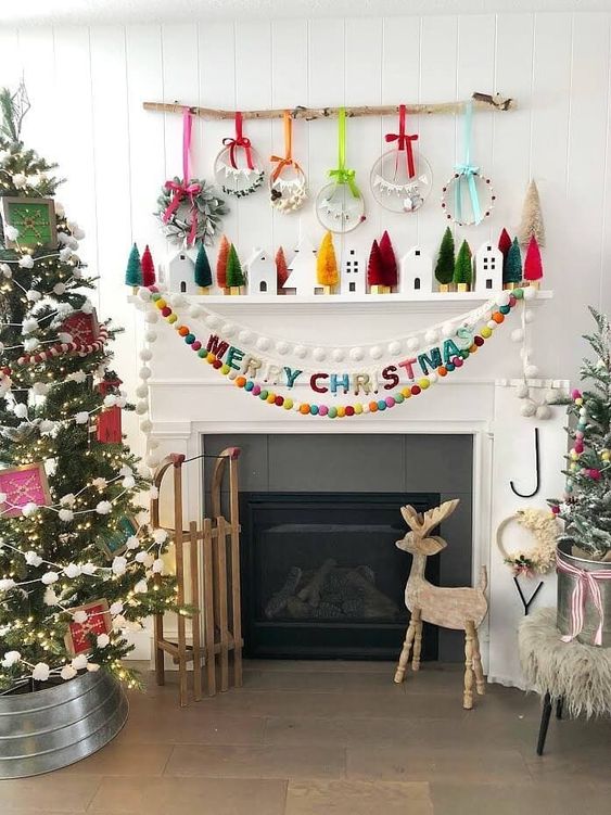 an out of the box Christmas mantel with colorful bottle cleaner trees, mini houses, an arrangement of mini wreaths and colorful pompom garlands