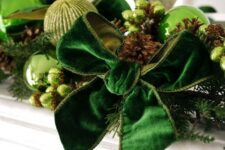 beautiful Christmas decor with light green and green glitter baubles, an emerald velvet bowm pinecones, beads and evergreens