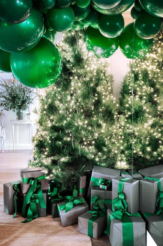 gorgeous Christmas decor with lots of lit up Christmas trees, emerald balloons and grey and green gift boxes is wow
