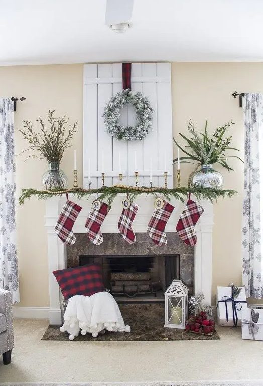 plaid stockings, an evergreen garland with wooden beads, candles in gilded candle holders and a snowy wreath over the mantel for a traditional Christmas look