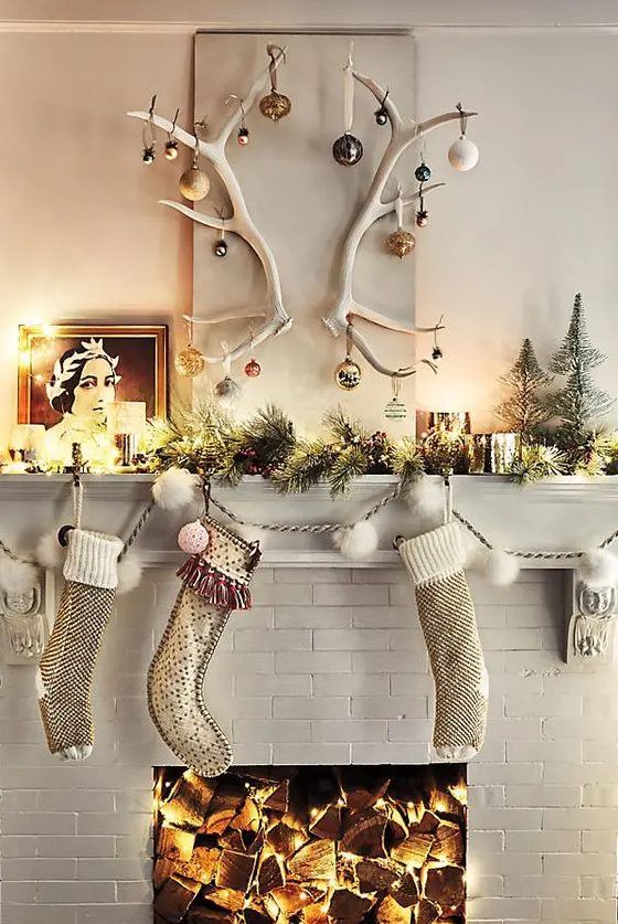 some stockings, an evergreen garland with lights, candles and antlers with Christmas ornaments for a super creative Christmas mantel look