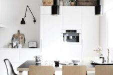 a Nordic kitchen with sleek white cabinets, black lamps, a black table and plywood chairs