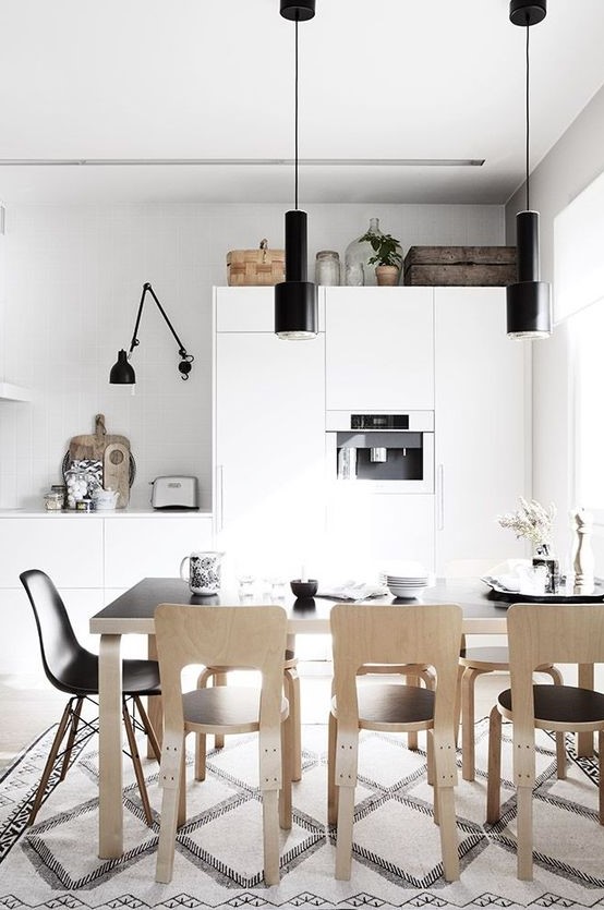 a Nordic kitchen with sleek white cabinets, black lamps, a black table and plywood chairs