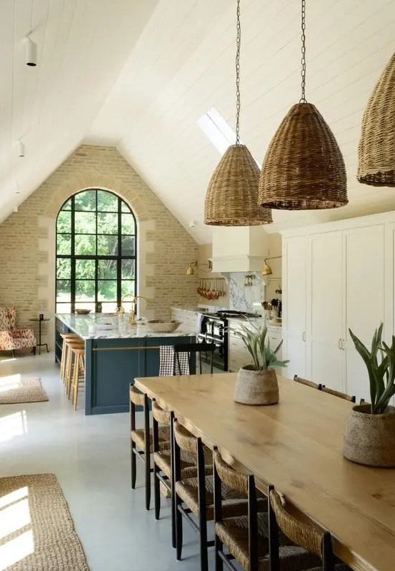 a barn kitchen with a stone accent wall, an arched window, white shaker style cabinets, a stone blue kitchen island and woven pendant lamps