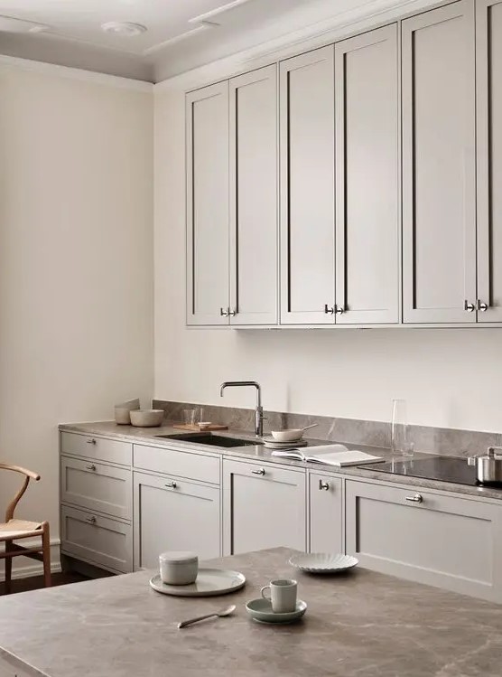 a beautiful Scandinavian greige kitchen with shaker cabinets, a brown stone countertop and a small backsplash plus a table with a matching tabletop