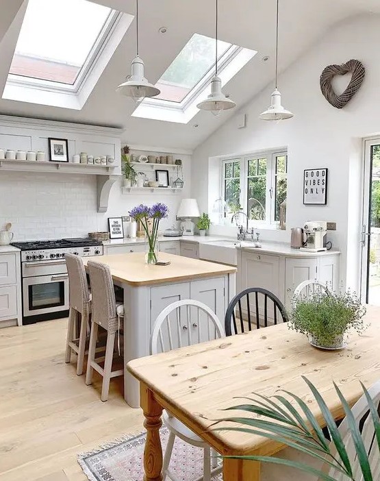 a beautiful attic cottage kitchen with shaker style cabinets, skylights, pendant lamps and a small kitchen island with woven stools