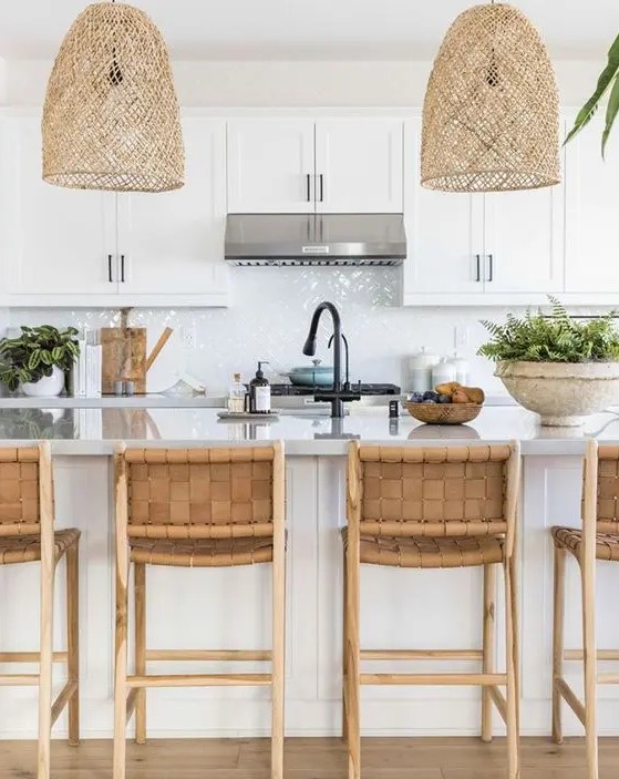 a beautiful beach kitchen in white, with shaker cabinets, a glossy white tile backsplash, a large kitchen island with woven stools and woven pendant lamps