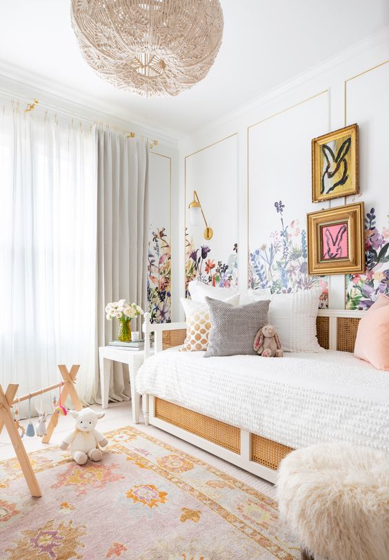 a beautiful girl's room with florals painted on the walls, a rattan bed with neutral bedding, a printed rug, a woven chandelier