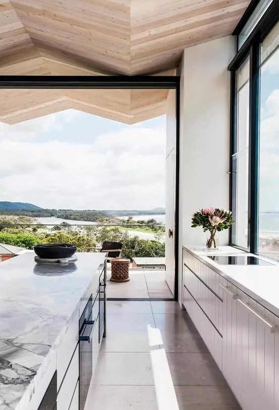 a beautiful light-filled contemporary kitchen with neutral cabinets, a kitchen island with a marble countertop and a glazed wall that can be removed
