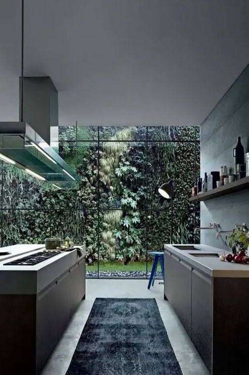 a beautiful minimalist kitchen with sleek dark cabinets, white stone countertops, an open shelf, a kitchen island and a glass wall that shows off greenery in a private garden