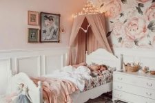 a beautiful pink girl’s bedroom with floral wallpaper, white paneling, vintage white furniture, a printed rug and a dusty pink canopy over the bed