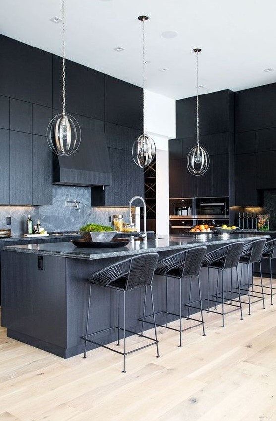 a black kitchen with textural cabinets, a kitchen island with a stone countertop and woven stools plus pendant lamps