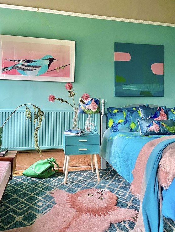 a blue and green bedroom with turquoise walls, a blue nightstand, a bed with pink and blue bedding and lovely artworks