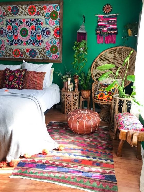 a boho maximalist bedroom with green walls, a colorful rug, a peacock chair, rattan and wooden furniture and a bold gallery wall