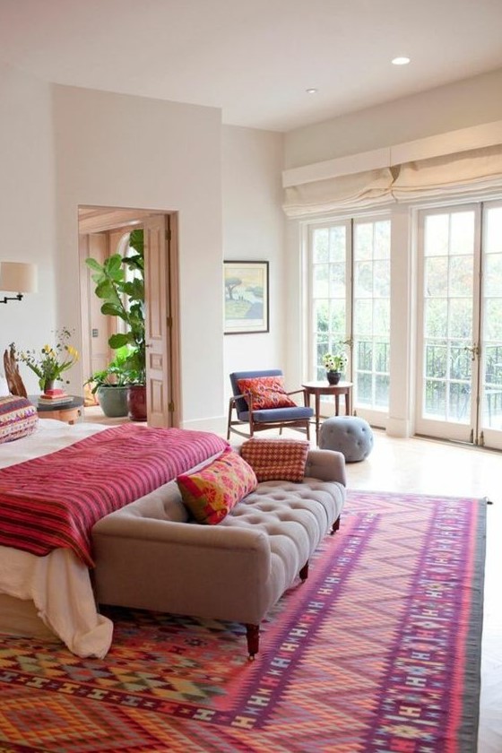 a bold bedroom with a colorful printed rug, a bold blanket and pillows that make this space super colorful