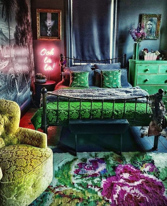 a bold maximalist bedroom with navy and grey walls, a forged bed, a green dresser, a neon light, statement artworks and a bold floral rug