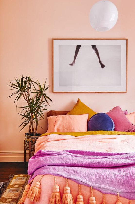 a bright bedroom with pink walls, colorful bedding and pillows, bright rugs and a statement artwork