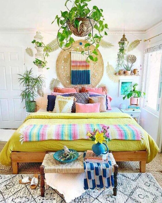 a bright boho bedroom with colorful bedding and pillows, a bold artwork and colorful macrame plus bright pots