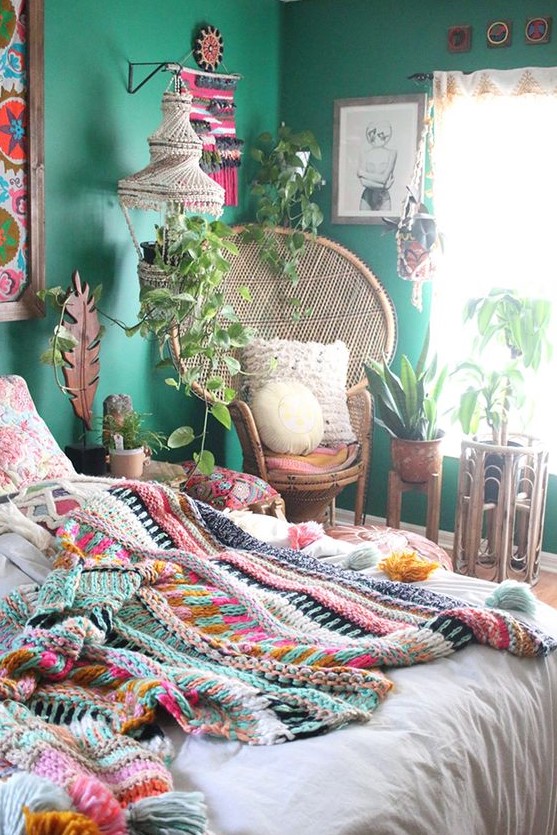 a bright boho bedroom with emerald walls, bold artworks and macrame, colorful bedding and a blanket and lots of potted plants