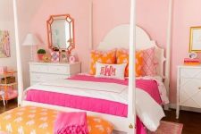 a bright pink girl’s room with a vintage bed with colorful bedding, a yellow bench with a pink blanket, a white chandelier and a pink printed rug