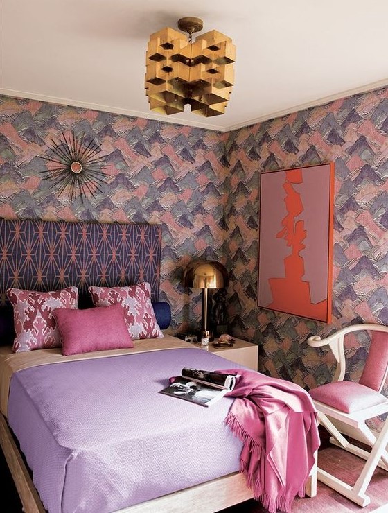 a bright romantic bedroom with brushstroke walls, a printed bed, pastel bedding, a pink chair, a gold sculptural chandelier