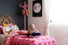 a catchy girl’s room with a black accent wall, a rattan bed with colorful bedding, artwork and a pink rack