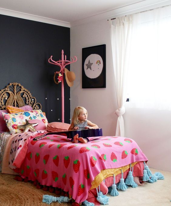 a catchy girl's room with a black accent wall, a rattan bed with colorful bedding, artwork and a pink rack
