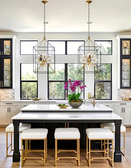 a chic glam kitchen with white and black cabinets, white marble tiles, cool sunburst chandeliers and gold and white stools