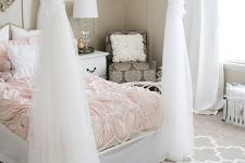 a chic greige girl’s room with a white bed with blush bedding, a taupe chair, layered rugs, pompoms and chic lamps
