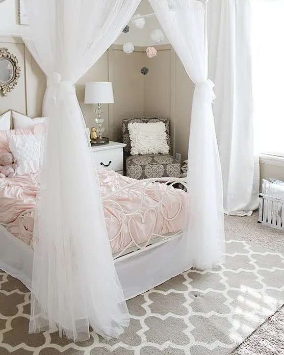 a chic greige girl's room with a white bed with blush bedding, a taupe chair, layered rugs, pompoms and chic lamps