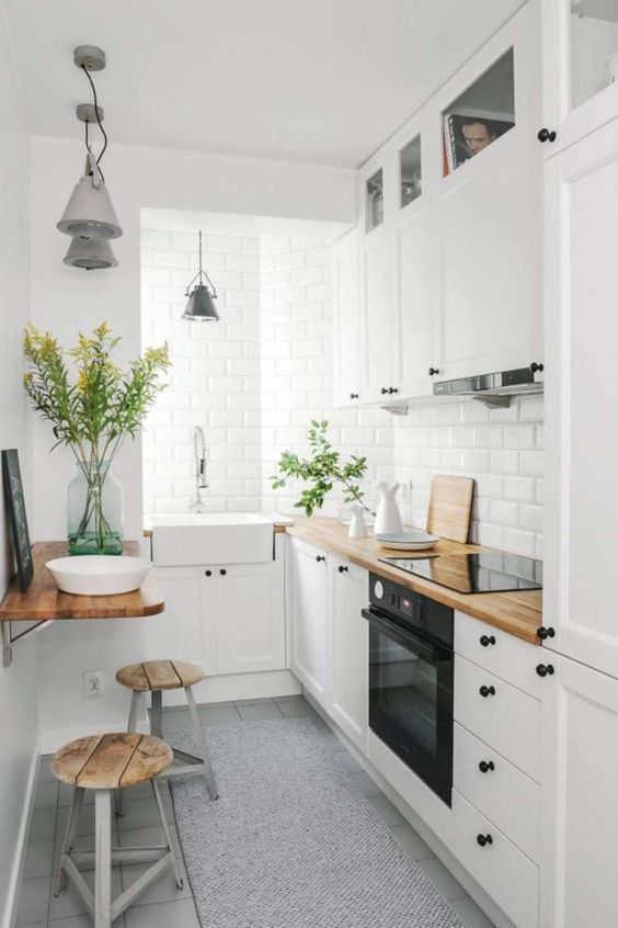 a chic white kitchen with butcherblock countertops, a folding table and stools and vintage pendant lamps