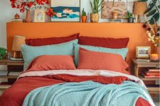 a colorful bedroom with a bed with an orange headboard, colorful bedding, a bright gallery wall and some bold blooms