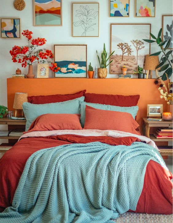 a colorful bedroom with a bed with an orange headboard, colorful bedding, a bright gallery wall and some bold blooms