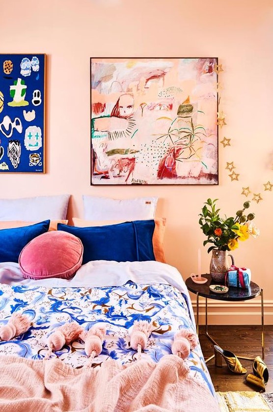 a colorful bedroom with blush walls, a bed with blue and pink bedding, bright artworks is a fun space