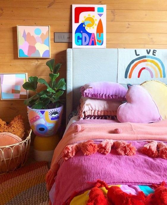 a colorful bedroom with super bright bedding and pillows, a colorful planter with painting and bright artworks on the wall